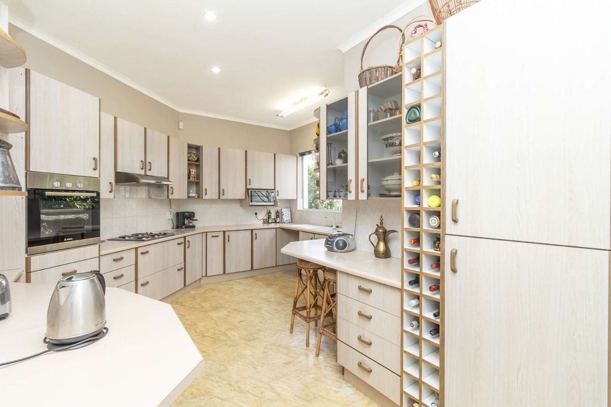 Spacious kitchen featuring light wood-grain cabinetry, integrated oven, gas hob, extractor fan, and a built-in wine rack with ample counter space.