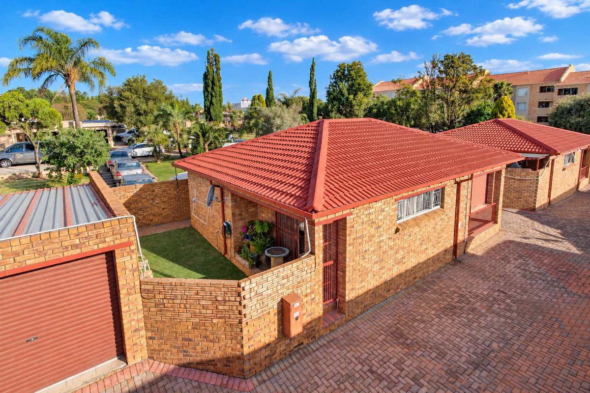An elevated view of a face brick townhouse featuring a tiled roof, private enclosed garden area, and paved driveway access.