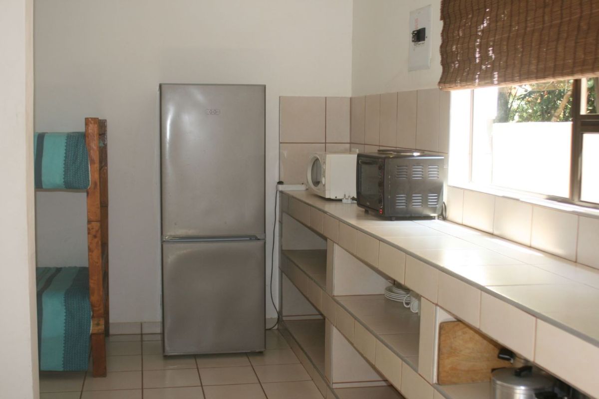 A functional kitchenette area featuring tiled countertops, open shelving, and tiled flooring, integrated within a multi-purpose room space.