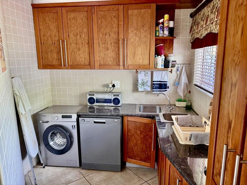 A functional laundry area featuring built-in wooden cabinetry, granite countertops, a stainless steel sink, and tiled finishes.