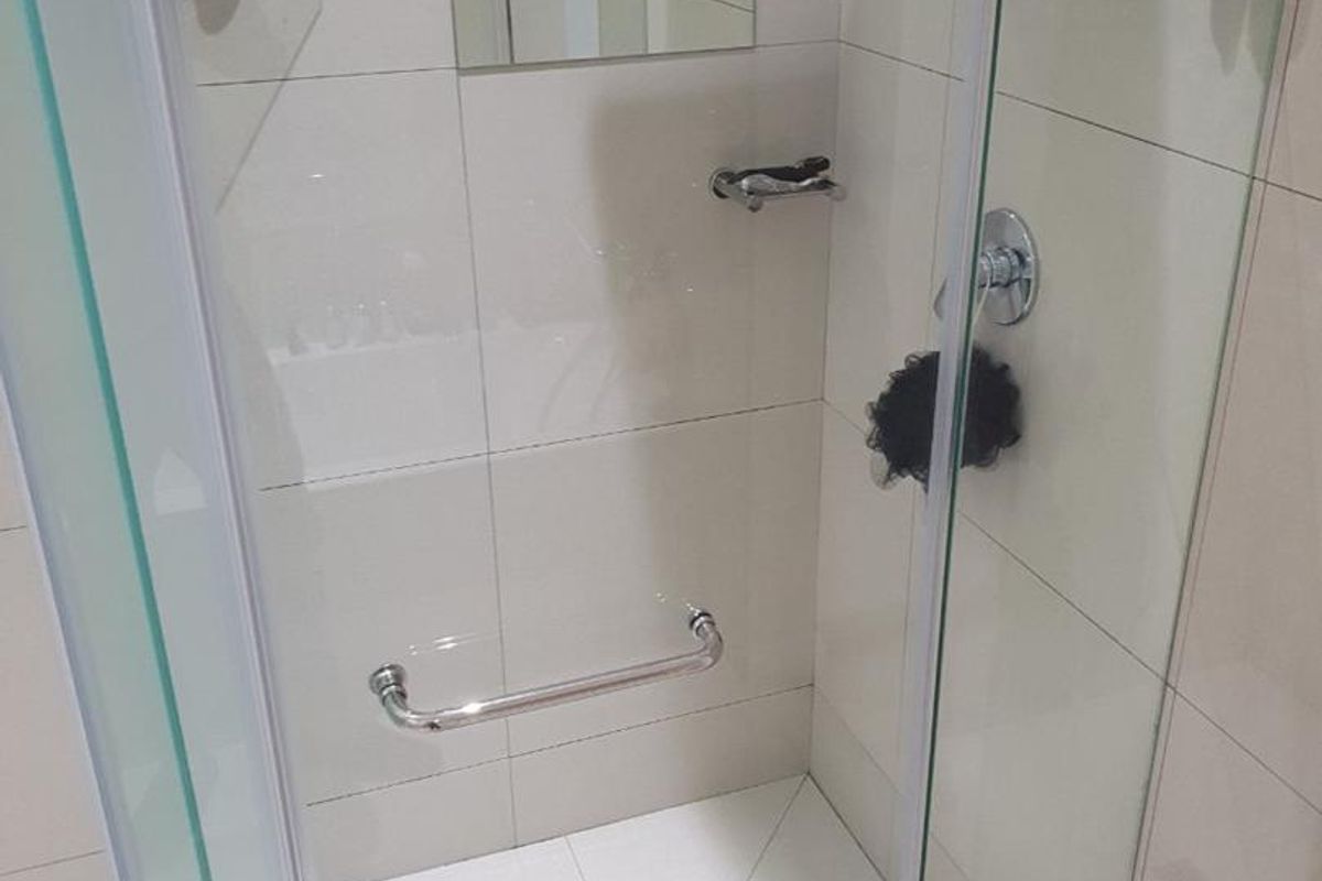 A modern shower enclosure featuring glass doors, tiled walls, a built-in grab rail, and integrated glass shelving.