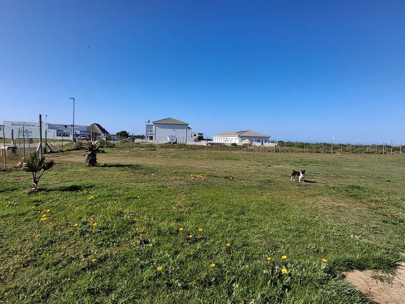 A vacant commercial land plot featuring open grass terrain, enclosed by wire mesh fencing with surrounding neighborhood infrastructure visible.