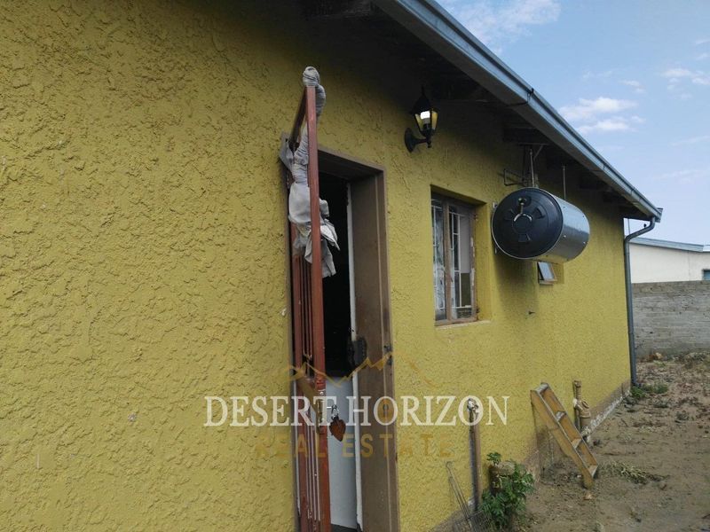 Rear exterior view of the property featuring a textured wall, security gate, and an externally mounted solar geyser unit.