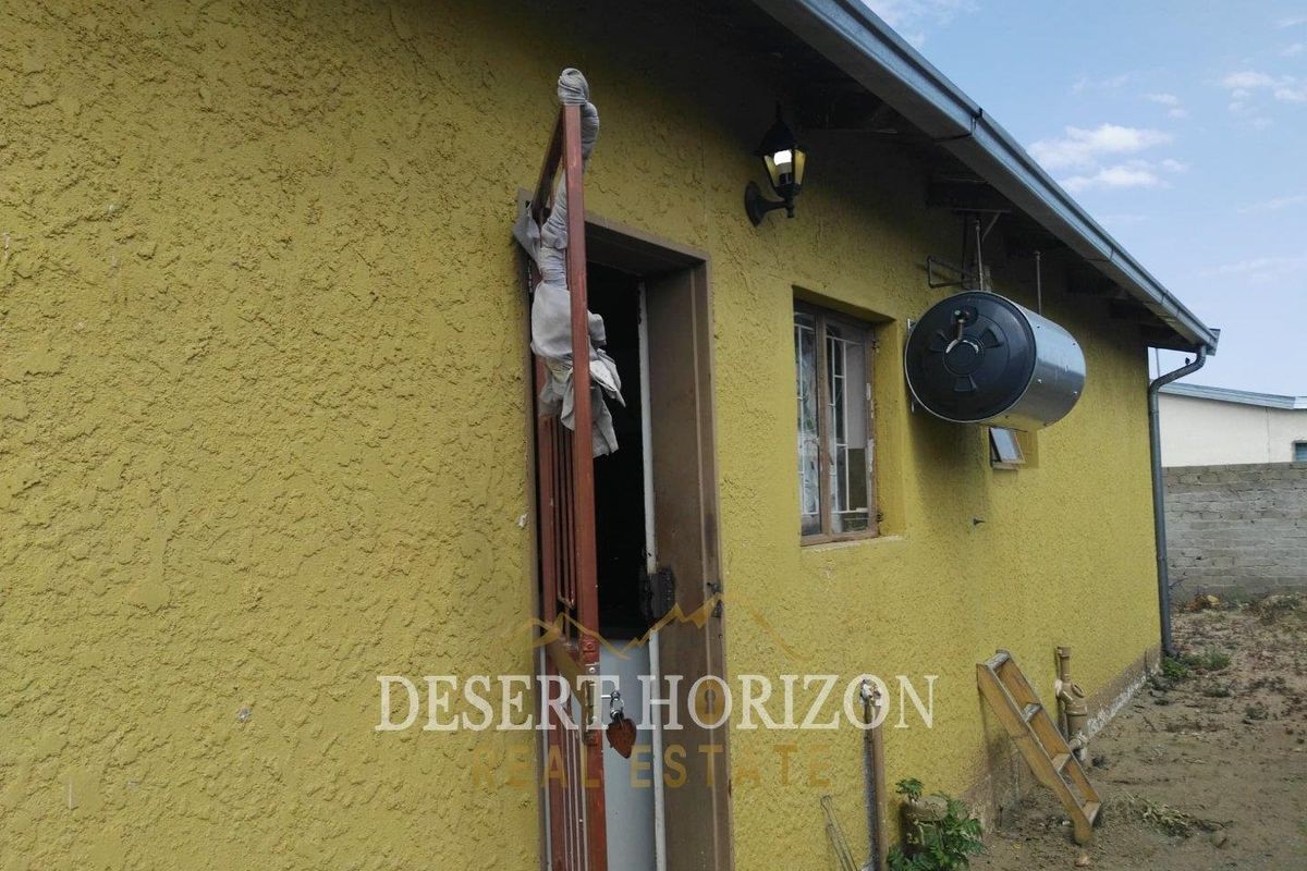 Rear exterior view of the property featuring a textured wall, security gate, and an externally mounted solar geyser unit.