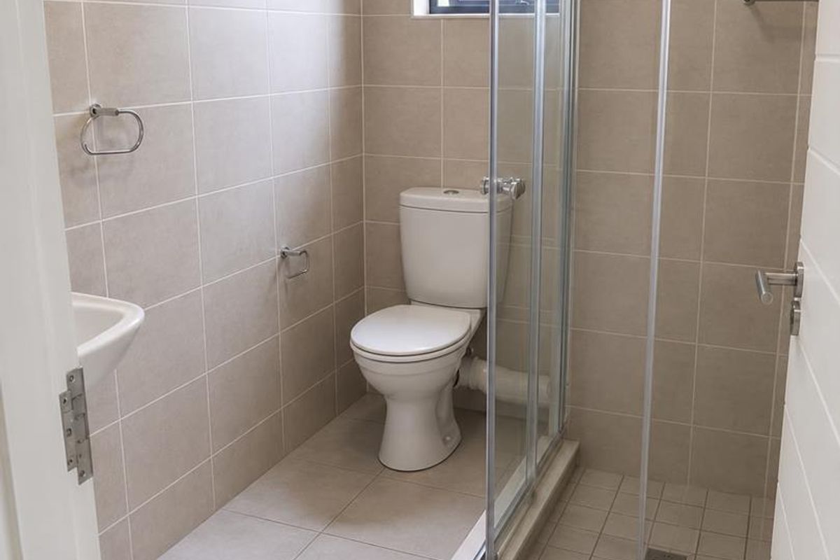 A clean, modern bathroom featuring neutral wall and floor tiles, a glass-enclosed shower, a white toilet, and a wall-mounted basin.