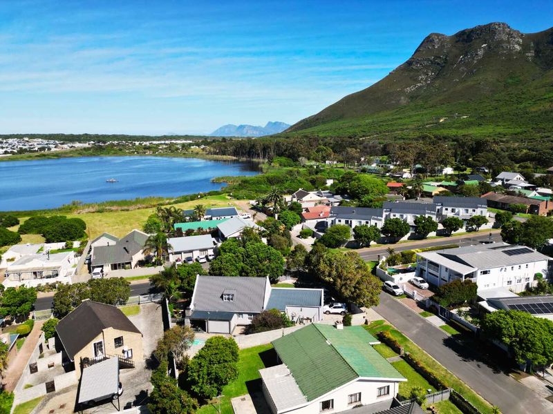 An aerial view of a residential neighborhood featuring pitched roof houses, paved streets, and proximity to a scenic lake and mountain landscape.