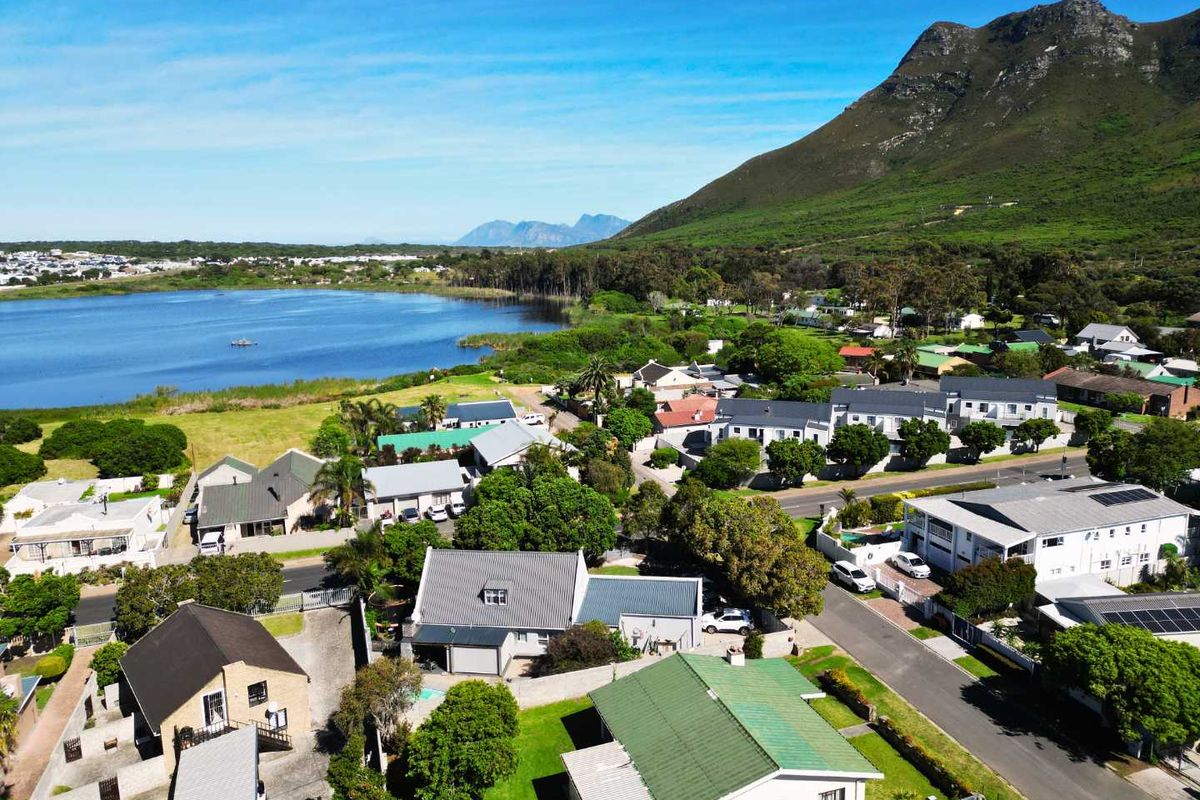 An aerial view of a residential neighborhood featuring pitched roof houses, paved streets, and proximity to a scenic lake and mountain landscape.