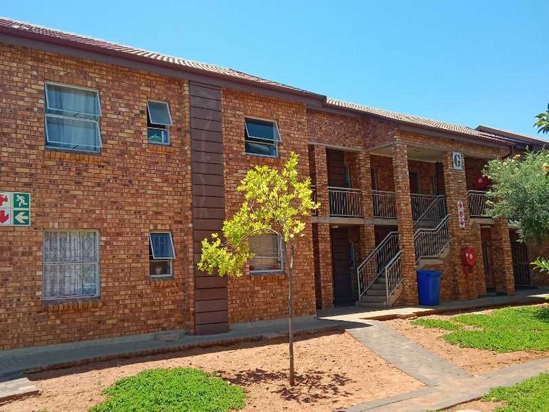 Exterior view of a multi-story apartment complex featuring face brick construction, metal staircases, and a paved walkway leading to the building entrance.