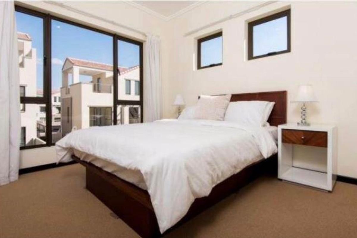 A bright bedroom featuring large windows with views of the surrounding apartment complex, neutral carpeting, and clean wall finishes.