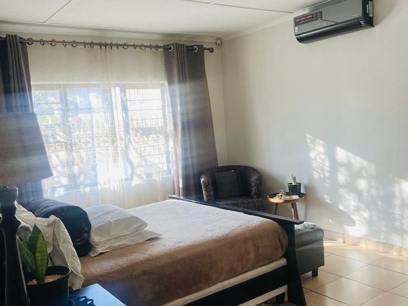 A bedroom featuring tiled flooring, a wall-mounted split-system air conditioner, and large windows with curtain rods.