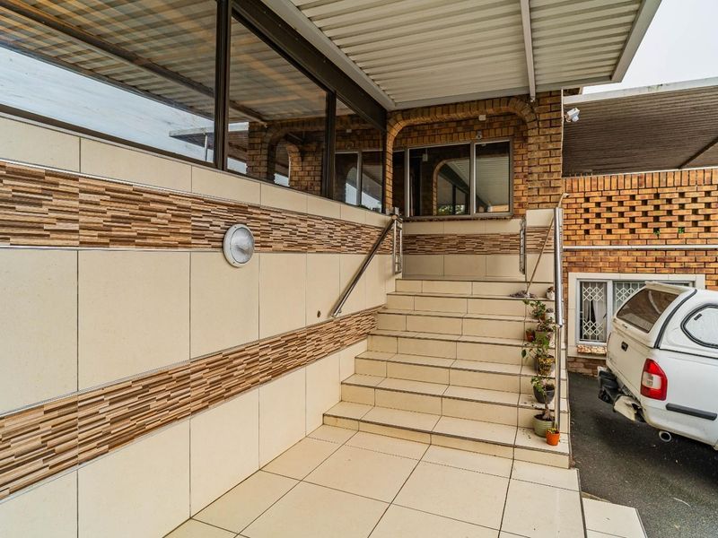 A well-maintained front entrance featuring a tiled staircase, decorative wall cladding, and a covered porch area with stainless steel handrails.