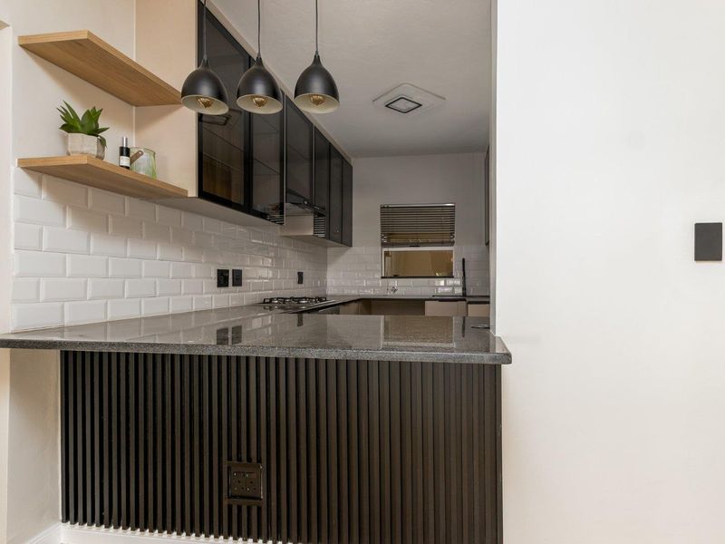 Modern kitchen featuring granite countertops, subway tile backsplash, sleek glass-fronted cabinetry, and a stylish slatted wood breakfast bar with pendant lighting.