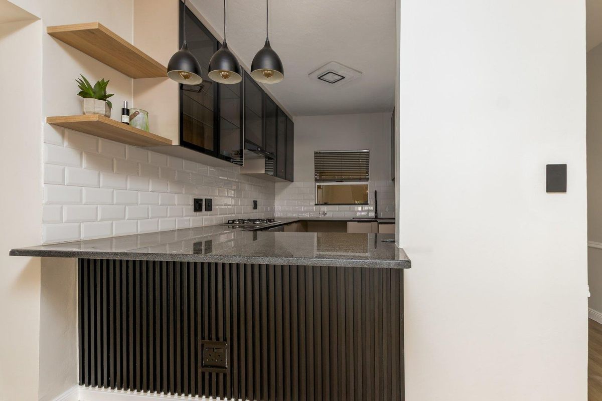 Modern kitchen featuring granite countertops, subway tile backsplash, sleek glass-fronted cabinetry, and a stylish slatted wood breakfast bar with pendant lighting.
