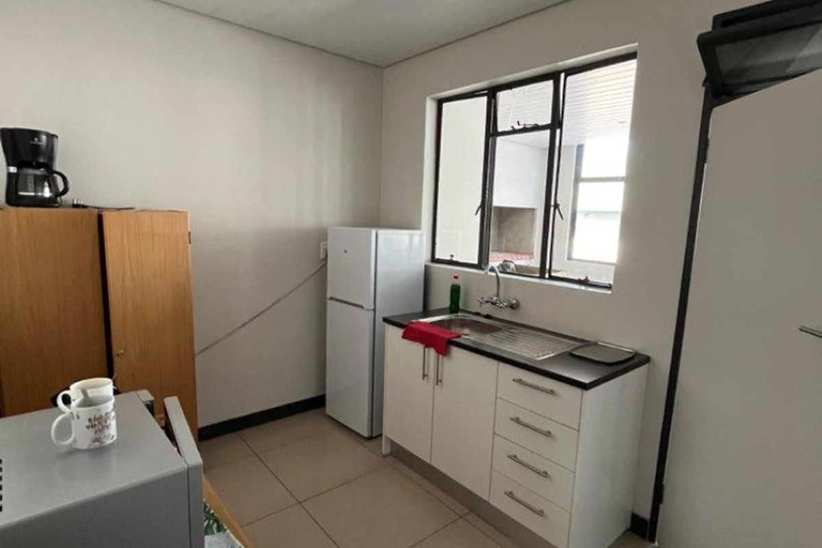 A compact kitchenette featuring a single-basin sink, built-in base cabinetry, tiled flooring, and a window providing natural light.