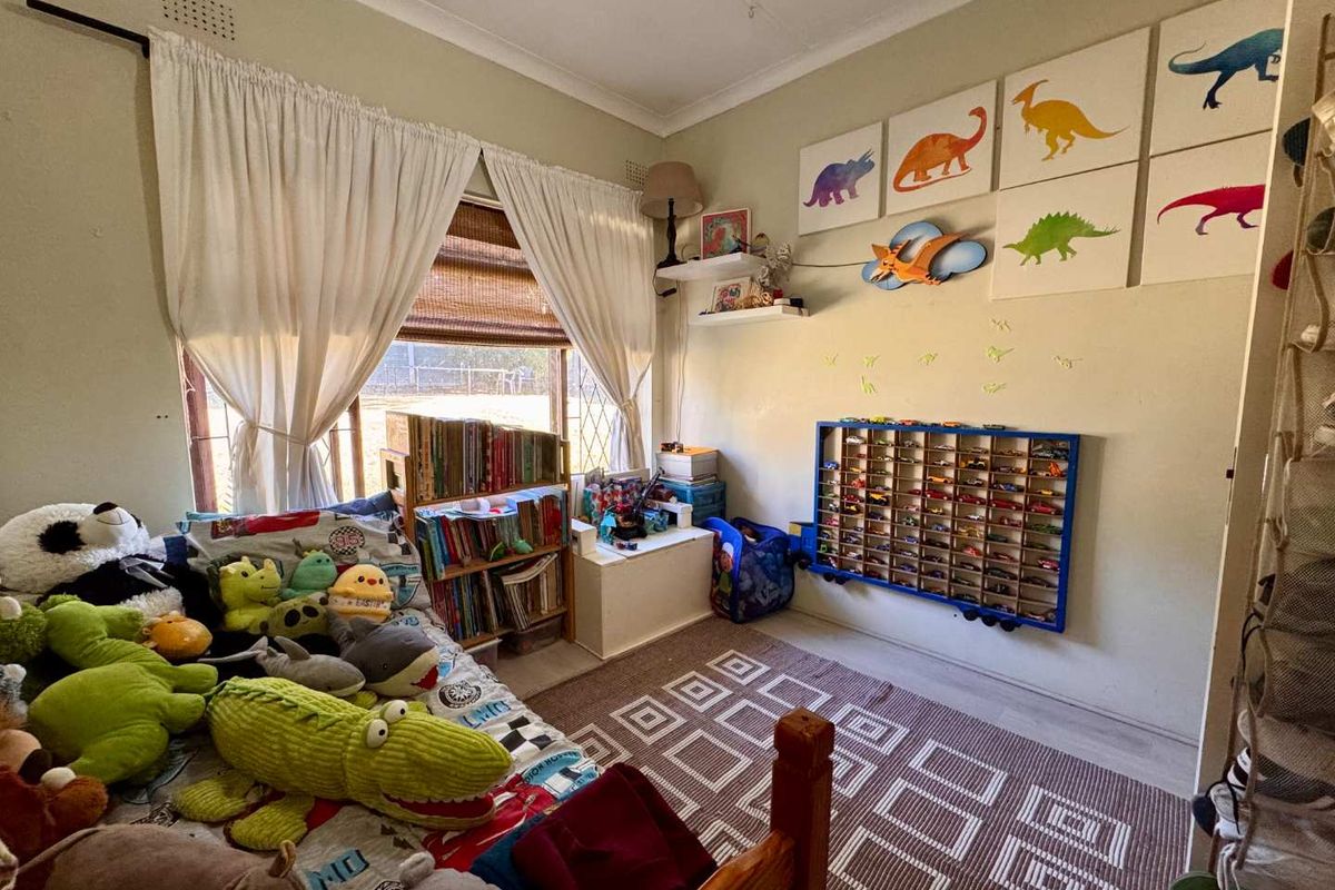 A bedroom featuring a window with curtains and wall-mounted shelving, currently utilized as a child's room.