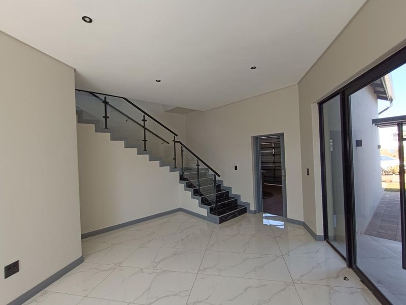 Modern entrance hall featuring polished marble-look floor tiles, a sleek staircase with glass balustrade, and large sliding glass doors leading to the exterior.