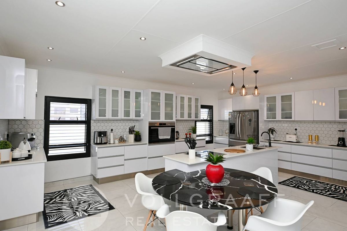 Modern kitchen featuring white cabinetry, a central island with a built-in hob, hexagonal tile backsplash, and integrated appliances.