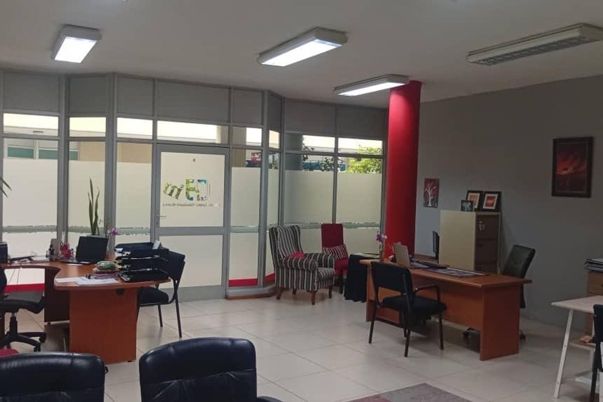 Open-plan office space featuring tiled flooring, aluminium-framed glass partitions, and integrated fluorescent lighting, providing a functional professional work environment.