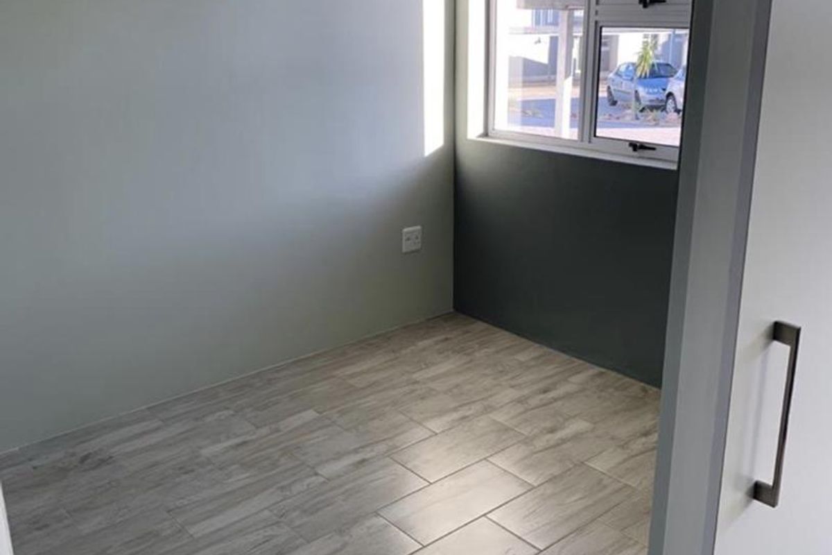 A bright, empty bedroom featuring modern wood-look tiled flooring, neutral wall tones, and a sliding door entrance.