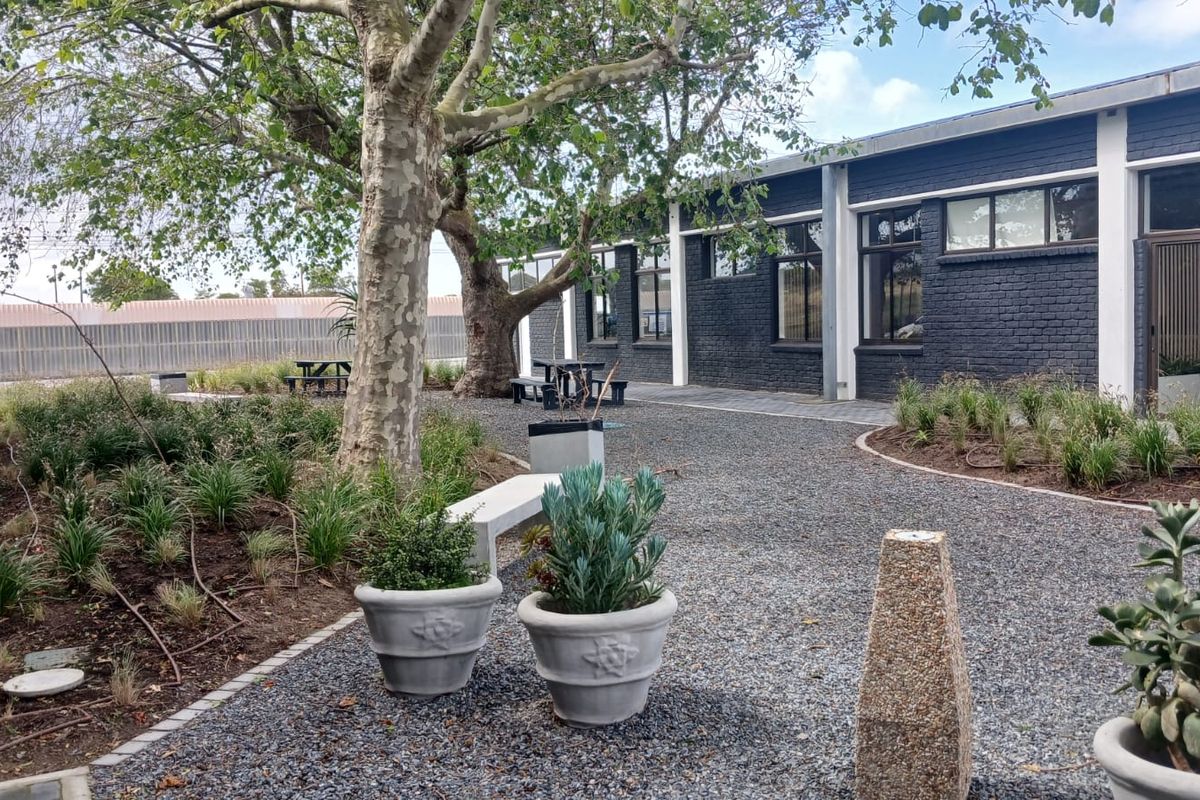 A well-maintained exterior rear area featuring a dark painted brick office facade, large windows, and landscaped gravel grounds with mature trees.