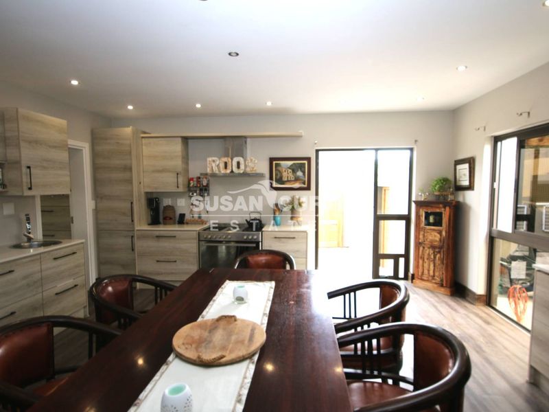 Open-plan kitchen and dining area featuring modern wood-look cabinetry, integrated appliances, recessed lighting, and direct access to the outdoor space via a sliding door.