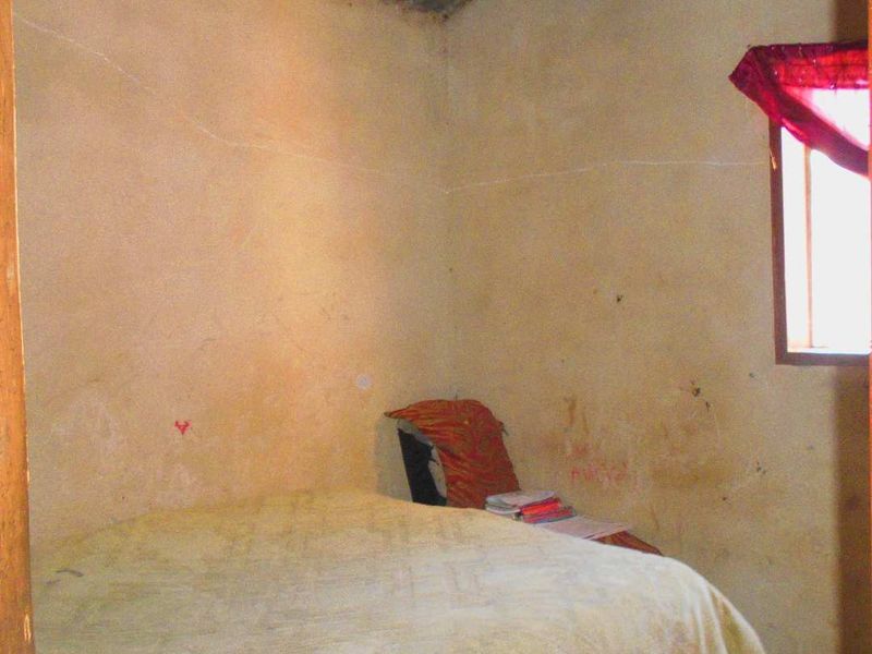 A basic bedroom featuring a corrugated metal ceiling and a single window, requiring significant cosmetic updates to the wall finishes.