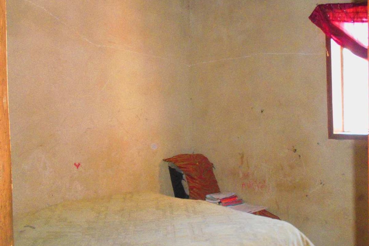 A basic bedroom featuring a corrugated metal ceiling and a single window, requiring significant cosmetic updates to the wall finishes.