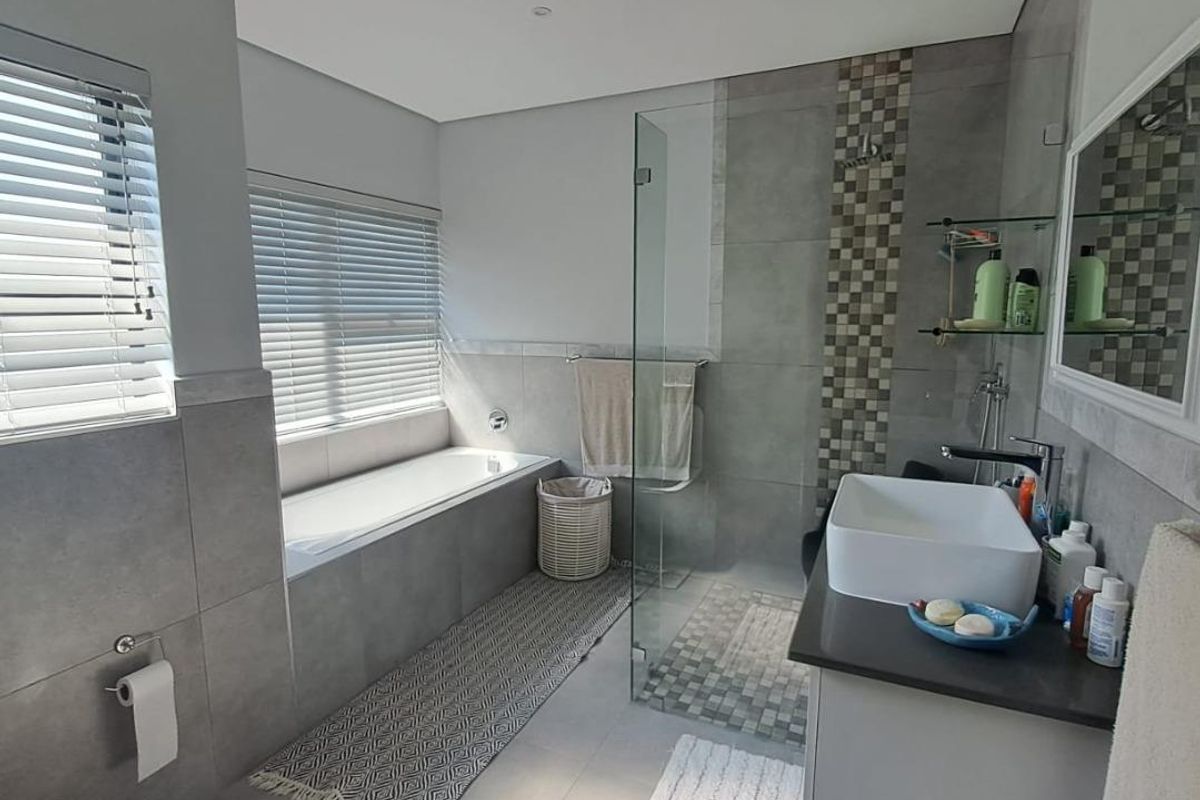 Modern bathroom featuring a built-in bathtub, glass-enclosed shower, vessel sink vanity, and neutral grey tiling throughout.