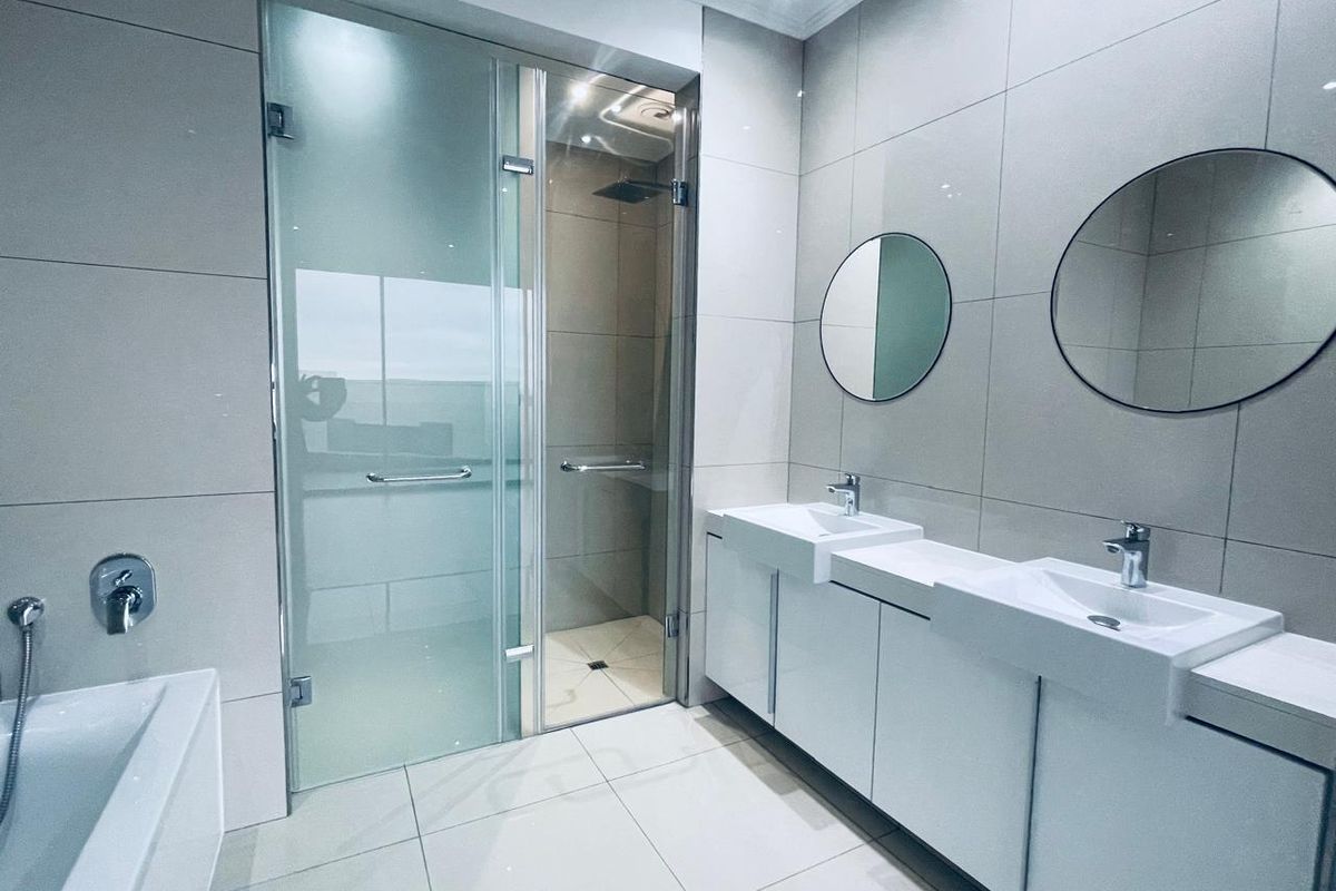 Modern bathroom featuring a double vanity with integrated sinks, a glass-enclosed walk-in shower, and large format floor-to-ceiling wall tiles.