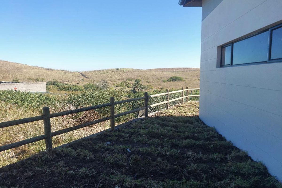 Rear exterior view of the property featuring a timber fence, plastered wall, and expansive views of the surrounding natural landscape.