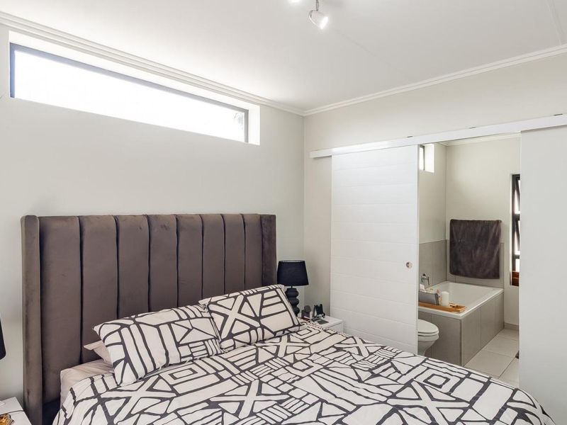 A well-lit bedroom featuring a modern sliding door providing direct access to an en-suite bathroom and a high-level clerestory window.