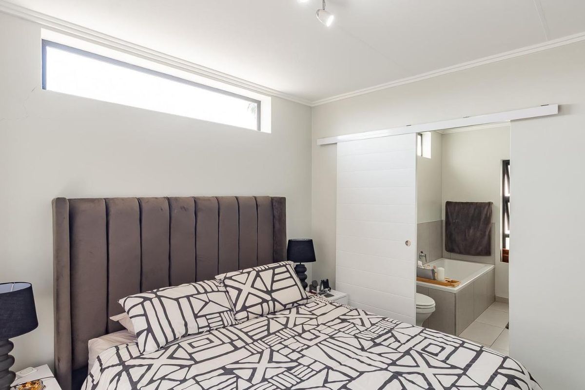 A well-lit bedroom featuring a modern sliding door providing direct access to an en-suite bathroom and a high-level clerestory window.