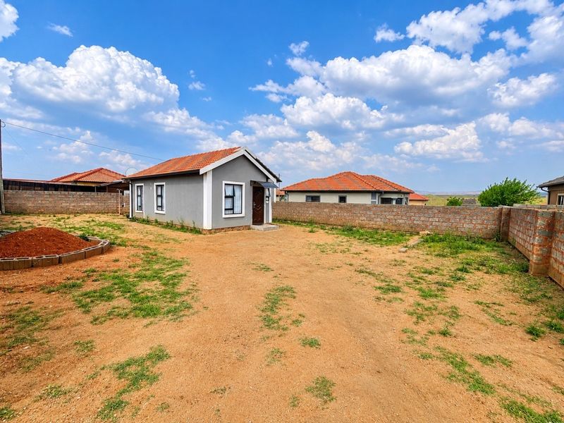 A detached single-story house featuring a terracotta tiled roof, set within a large, undeveloped plot enclosed by a perimeter brick wall.