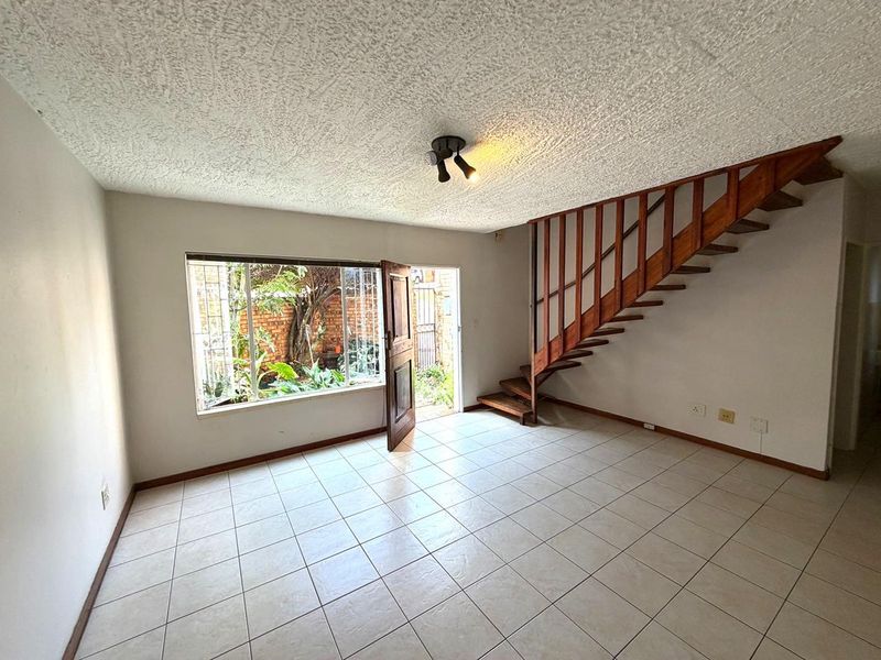 An open-plan living area featuring tiled flooring, a wooden staircase, and direct access to a private garden through a secure entrance.