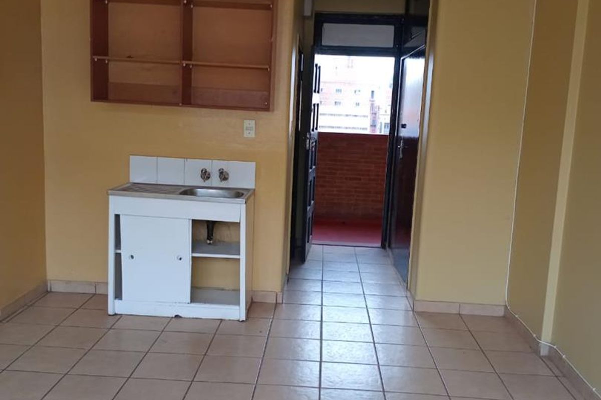 A basic kitchen area featuring a small sink unit, wall shelving, and ceramic floor tiles, leading out to a balcony.