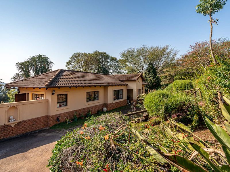 A well-maintained townhouse exterior featuring a tiled roof, brick and plaster facade, and a paved driveway surrounded by established garden landscaping.