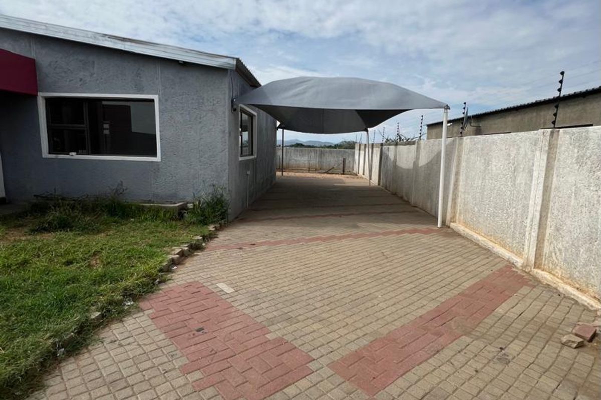 Side exterior view of the property featuring a paved driveway, a shade cloth carport, and perimeter boundary walls with electric fencing.