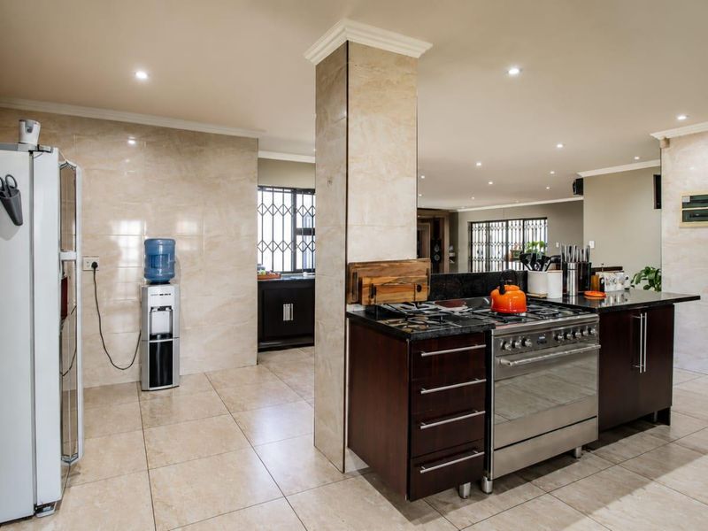 Spacious open-plan kitchen featuring dark wood cabinetry, granite countertops, a gas stove, and neutral tiled flooring with recessed lighting throughout.