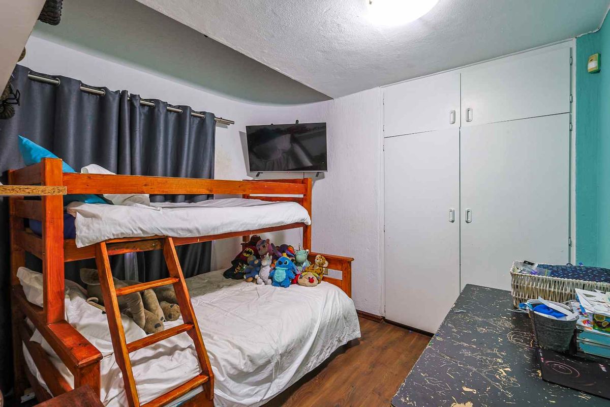 A bedroom featuring laminate flooring and a built-in wardrobe, showing signs of wear on the ceiling and walls.