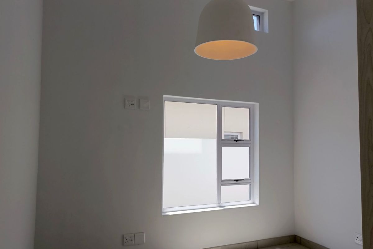 A bright, empty room featuring neutral tiled flooring, white walls, a modern pendant light fixture, and a window with aluminum frames.
