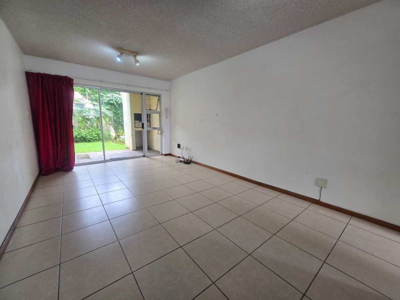 Spacious, empty living area featuring neutral tiled flooring and a large sliding glass door providing direct access to the outdoor patio and garden.