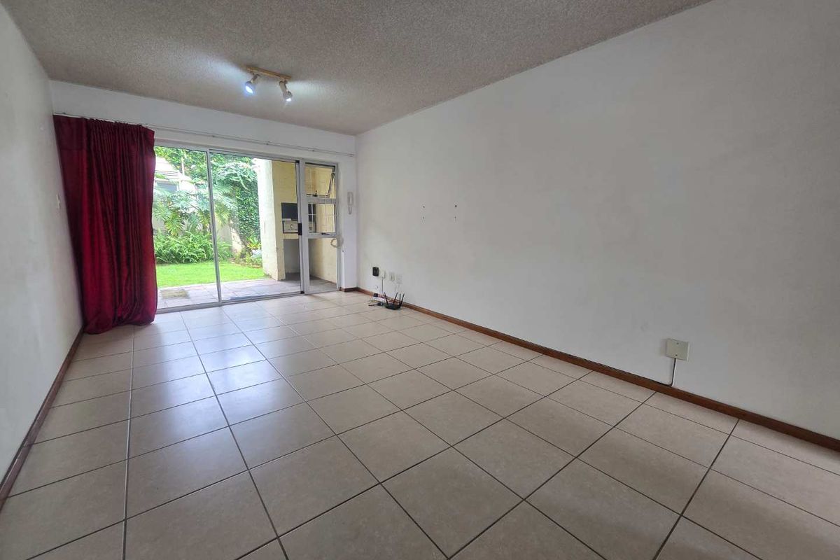 Spacious, empty living area featuring neutral tiled flooring and a large sliding glass door providing direct access to the outdoor patio and garden.