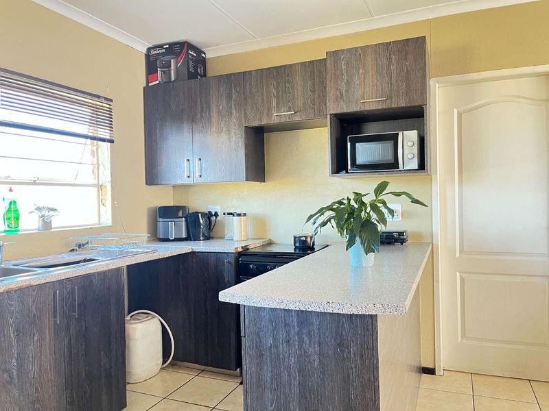 A functional kitchen featuring dark wood-look cabinetry, stone-effect countertops, built-in microwave, electric stove, and tiled flooring with natural light from the window.