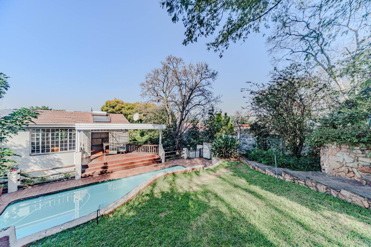 Rear exterior view featuring a swimming pool, wooden deck, and landscaped garden with stone retaining walls and mature trees.