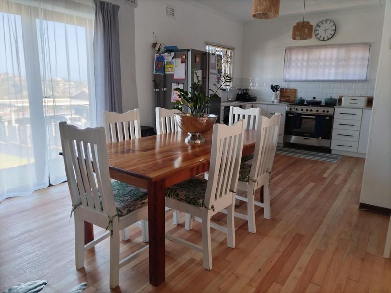 Open plan kitchen and dining area featuring hardwood flooring, white cabinetry with subway tile backsplash, and direct access to an outdoor space via sliding doors.