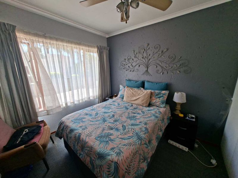 A cozy bedroom featuring a ceiling fan, textured accent wall, and large window with natural light.
