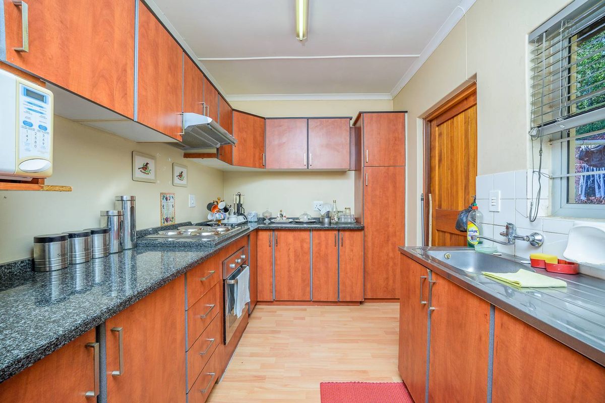 A functional kitchen featuring wood-look cabinetry, granite countertops, a built-in oven, hob, and extractor fan, with a stainless steel sink and tiled splashback.