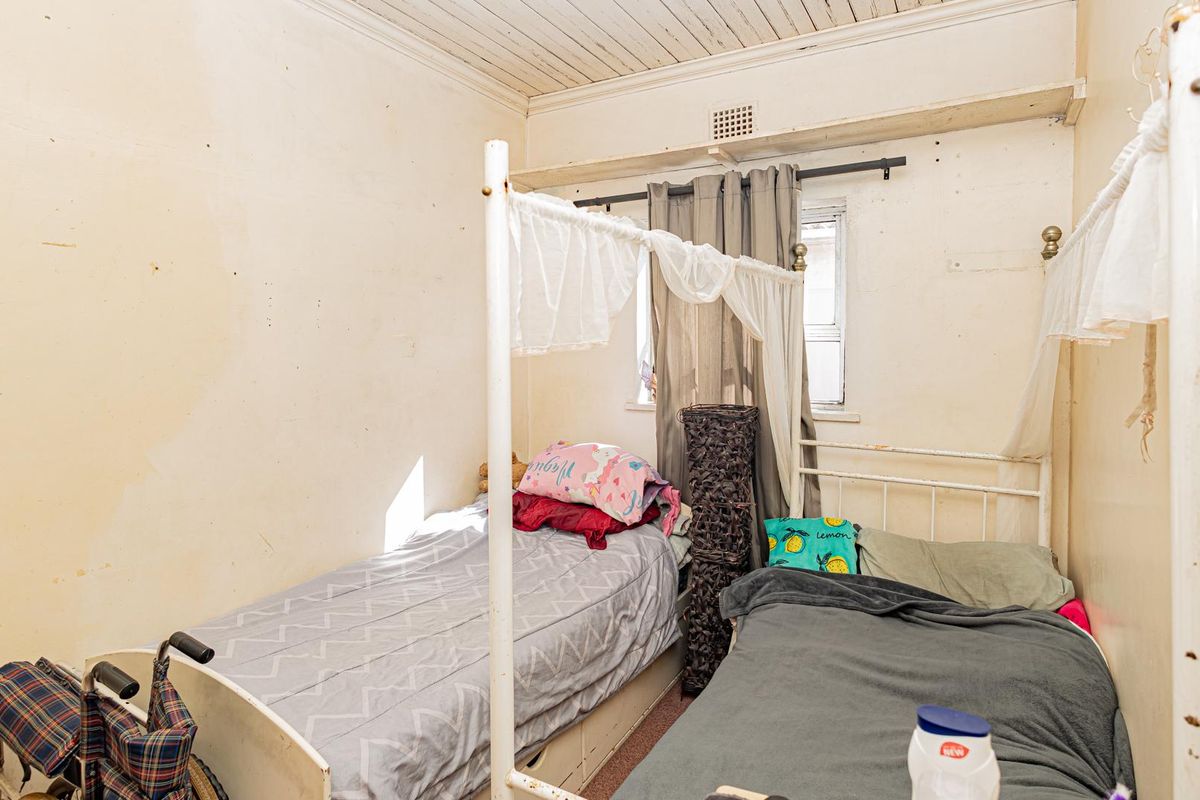 A compact bedroom featuring a timber ceiling and ventilation grille, currently requiring significant cosmetic updates and wall repairs to improve its overall condition.