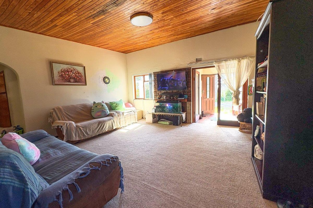 Spacious living room featuring a distinctive timber-clad ceiling, carpeted flooring, and a brick fireplace surround with direct access to the exterior.