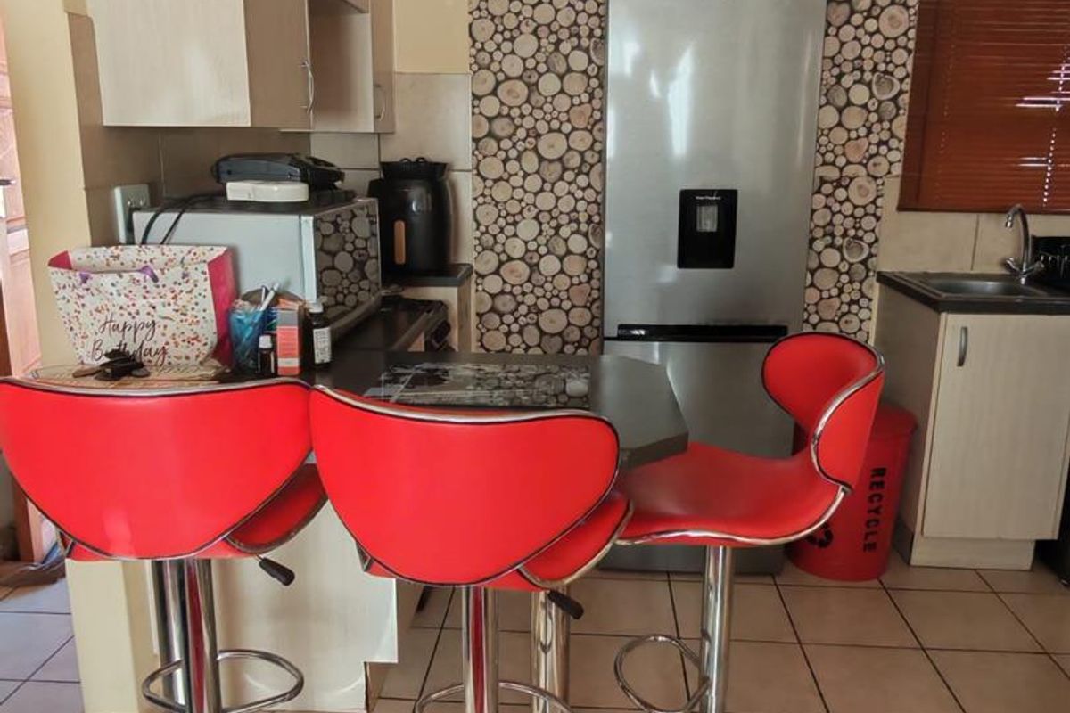 A compact kitchen featuring built-in cabinetry, tiled flooring, and a stainless steel sink, with a decorative feature wall behind the refrigerator area.